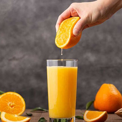 Hand squeezing an orange into a glass of orange juice with a dark background