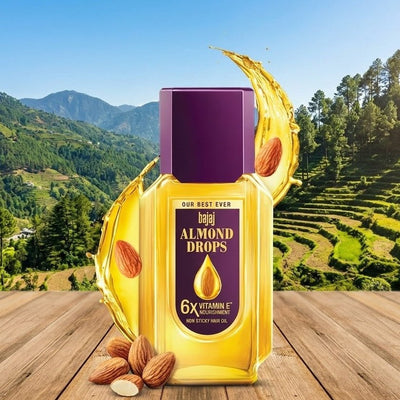 Bajaj Almond Drops bottle with almond nuts on a wooden surface with a mountainous background