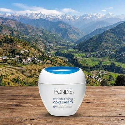 Pond's moisturizing cold cream jar on a wooden surface with a mountainous landscape in the background