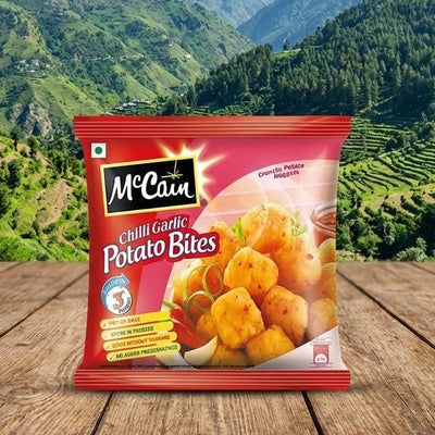 Mccain Chilli Garlic Potato Bites packet on a wooden surface with a mountainous landscape in the background