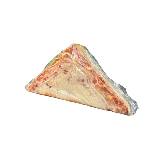 Triangular pizza slice wrapped in plastic on a metal surface with a store shelf in the background.