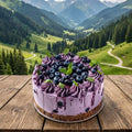 Purple cake with blueberries on a wooden table in front of a mountain landscape