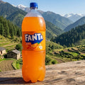 Fanta bottle on a wooden table with a scenic mountain landscape in the background