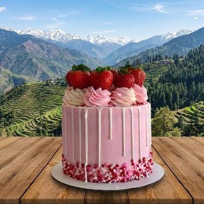 Pink cake with strawberries on a wooden table in front of a scenic mountain landscape