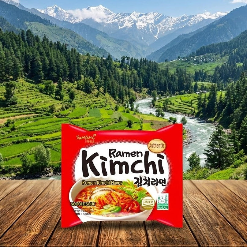 Packaged ramen with kimchi on a wooden surface in front of a scenic mountain landscape