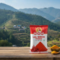 Bag of MDH Lal Mirch Powder with a scenic background of mountains and terraced fields.