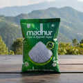 Green bag of Madhur sugar on a wooden surface with a mountainous landscape in the background