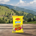 Maggi 2-Minute Noodles package on a wooden surface with a mountainous landscape in the background