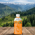 Orange juice bottle on a wooden surface with a scenic mountain background