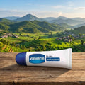 Vaseline lip care tube on a wooden surface with a scenic mountain landscape in the background