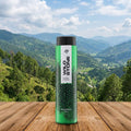 Green bottle with black cap on a wooden surface with a scenic mountain background