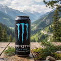 Monster Energy Absolutely Zero can on a wooden surface with a mountainous landscape in the background