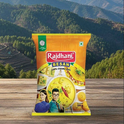 Rajdhani Besan packet on a wooden surface with a scenic mountain background