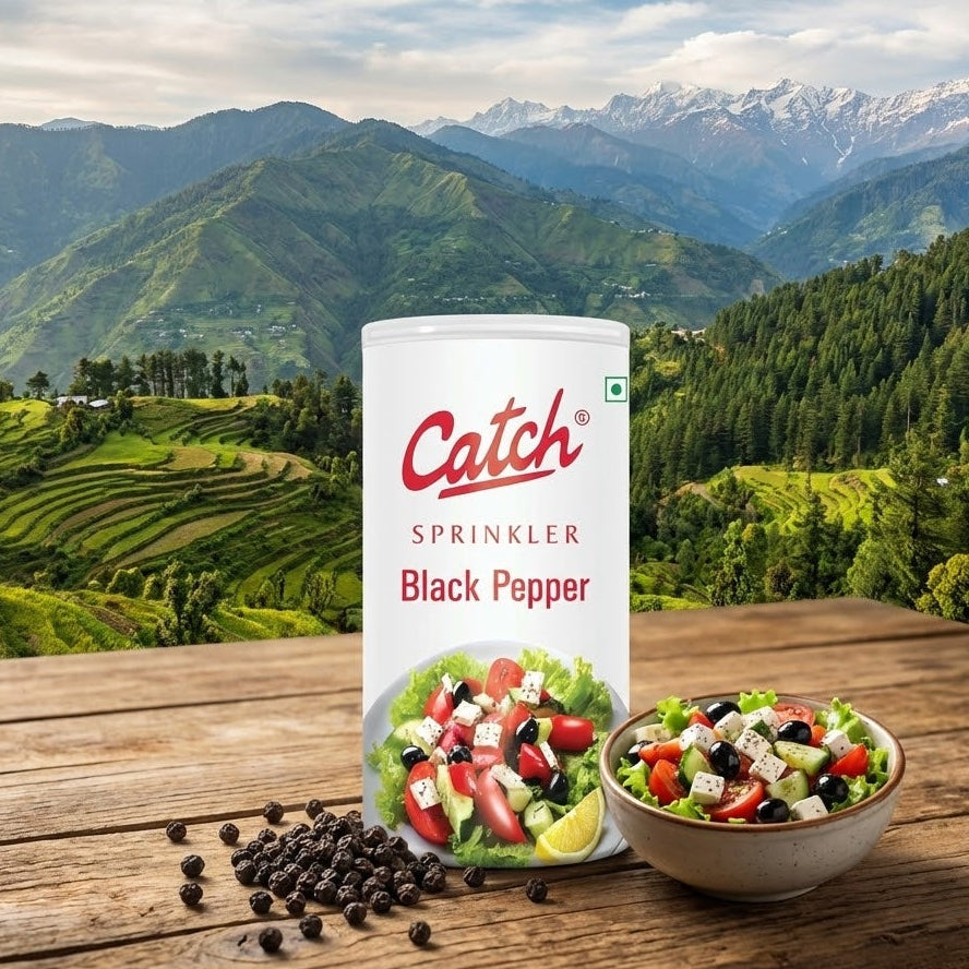 Can of Catch Black Pepper sprinkler with a bowl of salad on a wooden table with a mountainous landscape in the background