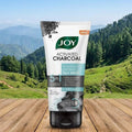 Joy Activated Charcoal face wash tube on a wooden surface with a scenic background