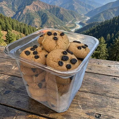 Clear container of chocolate chip cookies on a wooden surface with mountainous landscape in the background