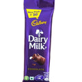 Hand holding a Cadbury Dairy Milk chocolate bar with colorful snacks in the background