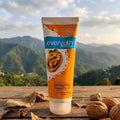 Tube of everyuth naturals Exfoliating Walnut Scrub with walnuts and leaves on a wooden surface with mountains in the background.