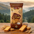Greet Premium Mix Pusik packaging with baked goods on a wooden table against a mountainous landscape.