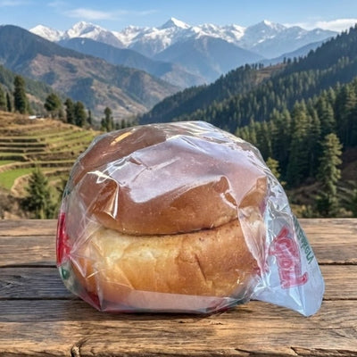 Two bread loaves in plastic wrap on a wooden surface with a mountainous landscape in the background.