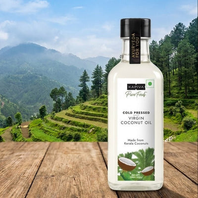 Bottle of Kapiva Virgin Coconut Oil on a wooden surface with a scenic mountain background