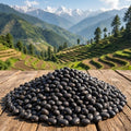 Pile of black beans on a wooden surface with a scenic mountain landscape in the background