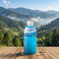 Blue bottle of Mogu Mogu on a wooden table with a scenic mountain landscape in the background
