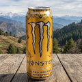 Monster Energy Ultra Golden Pineapple can on a wooden surface with a mountainous landscape in the background