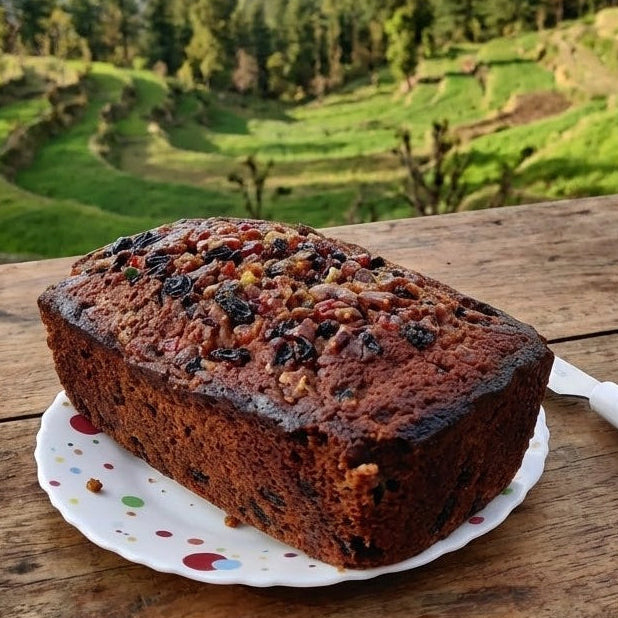 Loaf of fruit cake on a wooden table with a scenic background of mountains and terraced fields.
