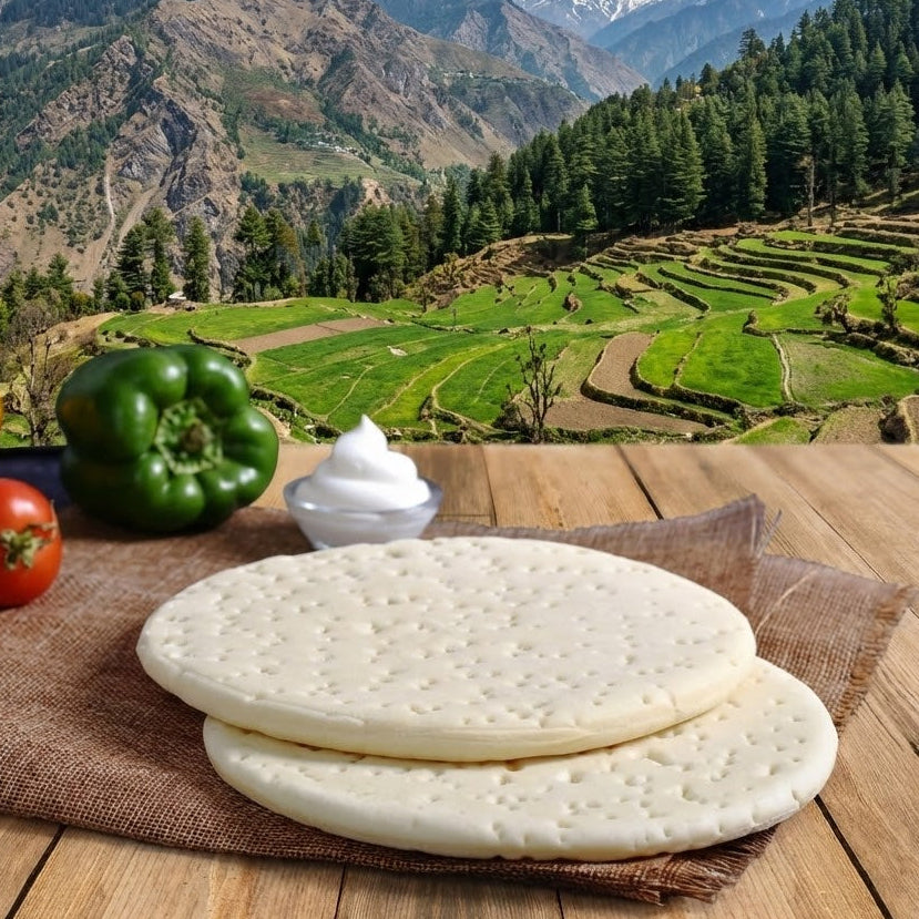 Stack of flatbreads on a wooden table with vegetables and a scenic mountain landscape in the background