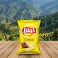 Lay's Classic potato chips packet on a wooden surface with a mountainous landscape in the background