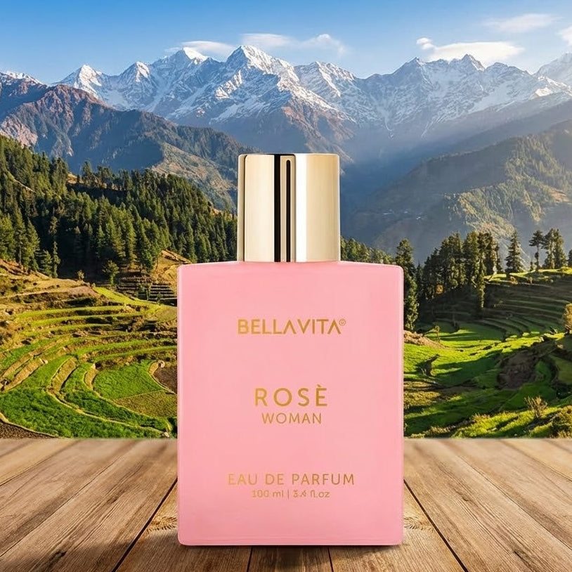 Pink Bellavita Rose perfume bottle on a wooden surface with a mountainous landscape in the background