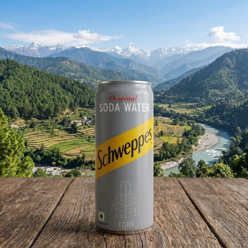 Schweppes soda water can on a wooden surface with a scenic mountain view in the background