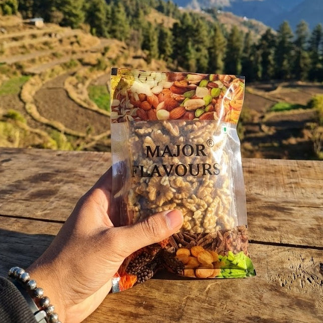 Hand holding a packet of 'Major Flavours' snacks with a scenic mountain view in the background