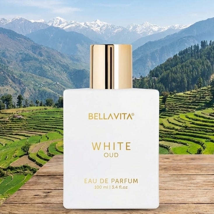 Bellavita White Oud perfume bottle on a wooden surface with a scenic mountain background