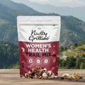 Nutty Gritties Women's Health Trail Mix package on a wooden surface with a mountainous landscape in the background